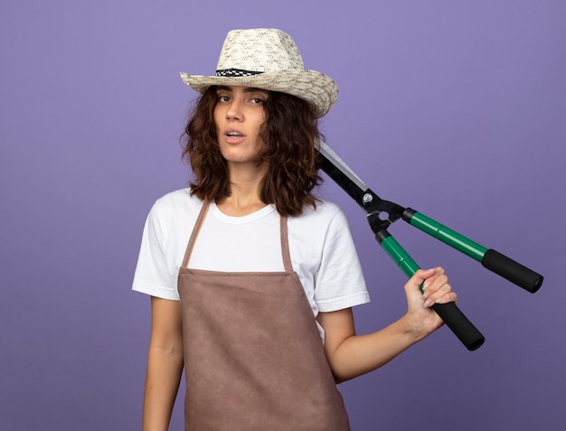 Confiant jeune jardinière en uniforme portant chapeau de jardinage tenant une tondeuse