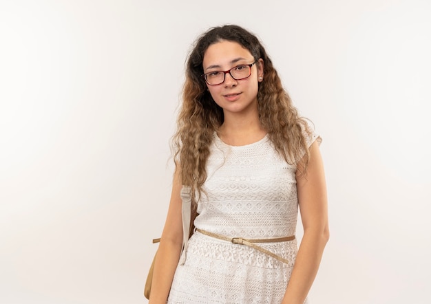 Photo gratuite confiant jeune jolie écolière portant des lunettes et sac à dos debout et regardant isolé sur blanc avec copie espace