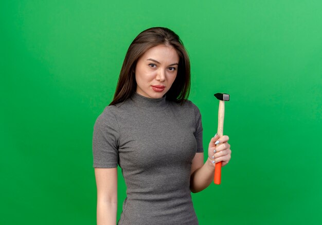 Confiant jeune jolie femme tenant un marteau isolé sur fond vert avec espace copie