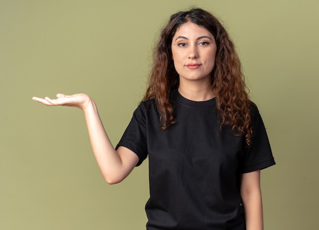 Confiant jeune jolie fille caucasienne pointant avec la main sur le côté isolé sur mur vert olive