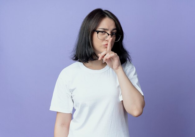 Confiant jeune jolie fille caucasienne portant des lunettes faisant le geste de silence isolé sur fond violet avec copie espace