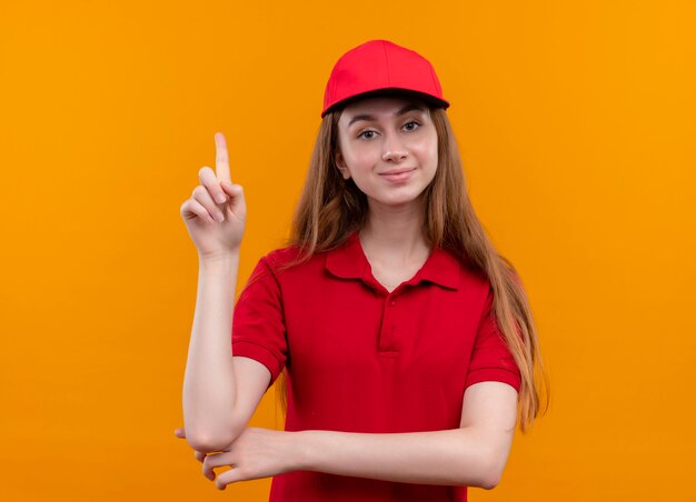 Confiant jeune livreuse en uniforme rouge avec doigt levé sur l'espace orange isolé