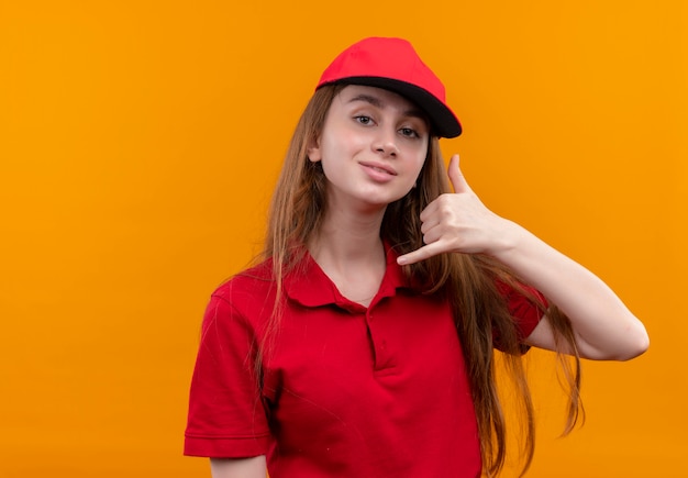 Photo gratuite confiant jeune livreuse en uniforme rouge faisant le geste d'appel sur l'espace orange isolé avec copie espace