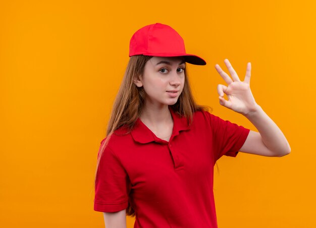 Confiant jeune livreuse en uniforme rouge faisant signe ok sur espace orange isolé avec copie espace