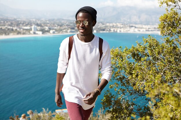 Confiant jeune voyageur masculin avec sac à dos debout sur la montagne au bord de la mer