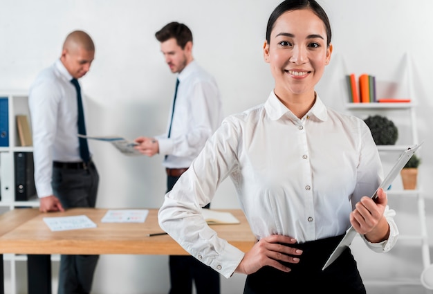 Confiant, souriant, jeune femme affaires, tenant presse-papiers dans main, à, deux, homme affaires, debout, à, toile de fond