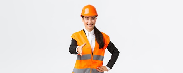 Confiant succès femme architecte leader de la construction dans la veste réfléchissante de casque de sécurité tend la main pour la poignée de main saluant les partenaires commerciaux dans la zone de construction debout fond blanc