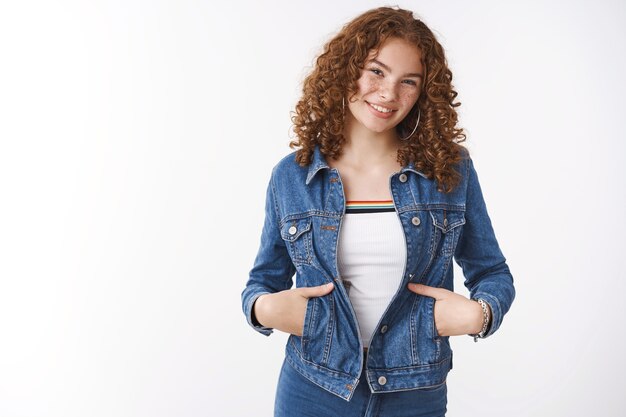 Confiante charmante petite amie rousse des années 20 portant une veste en jean sortir marcher tenir les poches des mains souriant largement rencontrer un ami avoir de petites discussions dans la rue debout fond blanc souriant joyeusement