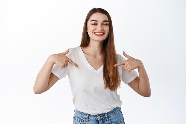 Confiante fille souriante pointant vers elle-même montrant le logo du centre autopromotion démontrer le texte promotionnel debout sur fond blanc