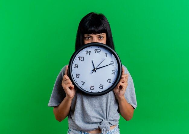 Confiante jeune femme caucasienne brune tient et regarde par-dessus l'horloge