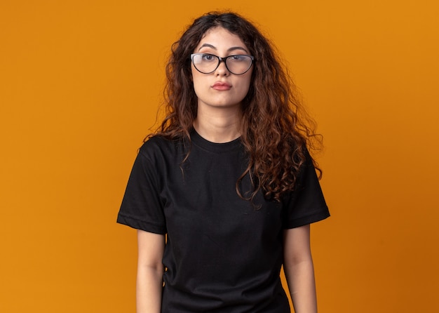 Confiante jeune jolie femme portant des lunettes regardant l'avant isolé sur un mur orange avec espace de copie