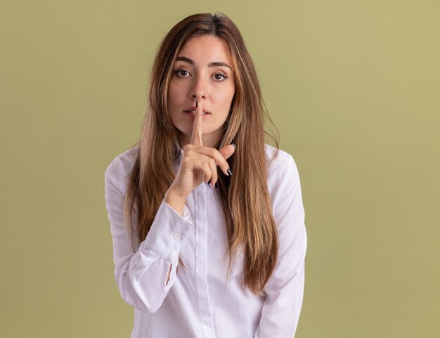 Confiante jeune jolie fille caucasienne faisant un geste de silence isolé sur un mur vert olive avec espace pour copie