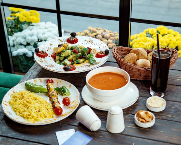 Une configuration de déjeuner avec des brochettes de riz et de poulet salade grecque et soupe aux lentilles
