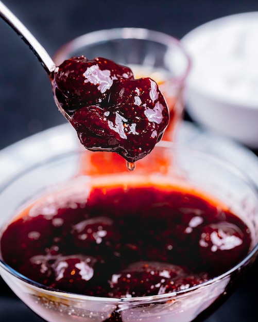 Confiture de fraises coulant de la cuillère dans la vue latérale de la verrerie