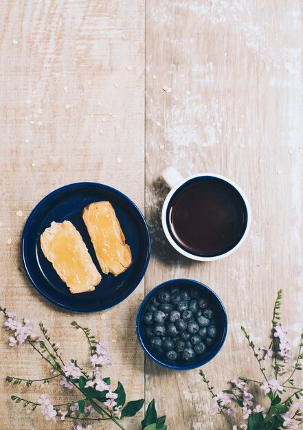 Confiture tartinée sur du pain grillé; myrtilles; tasse à café et fleurs roses sur table en bois