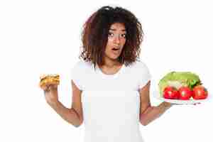 Photo gratuite confondre la jeune femme africaine en choisissant entre burger et légumes.