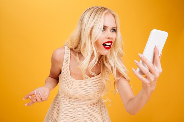 Confondu choqué jeune femme blonde à l'aide de téléphone portable.