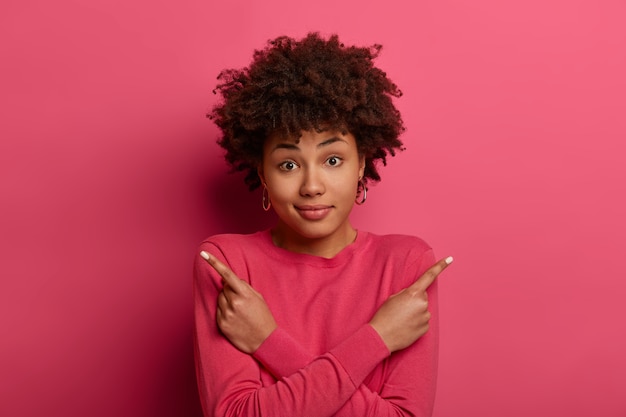 Photo gratuite confus belle jeune femme afro-américaine croise les bras sur le corps, pointe à gauche et à droite, dans des directions différentes, choisit la meilleure option