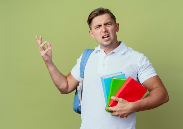 Confus jeune étudiant beau mâle portant sac à dos tenant des livres isolés sur fond vert olive