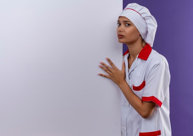 Confus jeune femme cuisinier portant l'uniforme de chef tenant un mur blanc sur un mur isolé avec copie espace