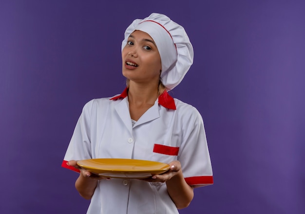 Confus jeune femme cuisinier portant un uniforme de chef tenant la plaque sur un mur isolé avec copie espace