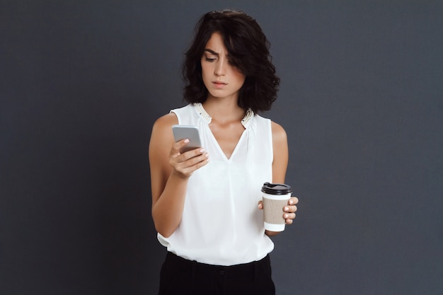 Confus jeune femme tenant son téléphone et son café dans les mains