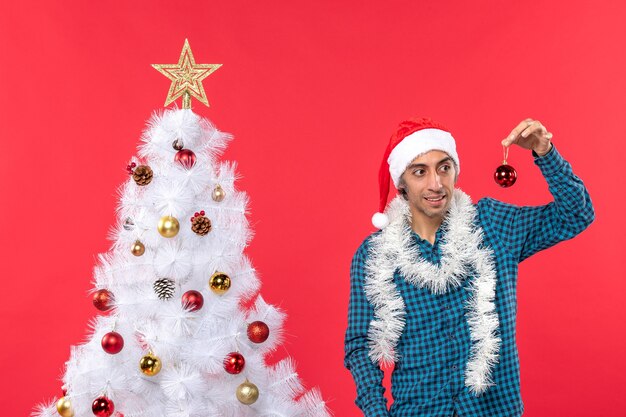 Confus jeune homme avec chapeau de père Noël dans une chemise rayée bleue et montrant l'accessoire de décoration