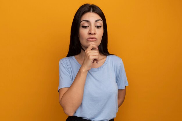 Confus jolie brune caucasienne fille tient le menton et regarde vers le bas sur l'orange