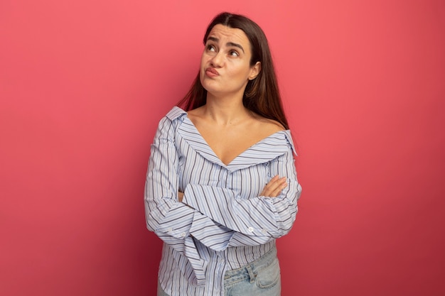 Confus jolie femme caucasienne se tient avec les bras croisés à côté sur rose