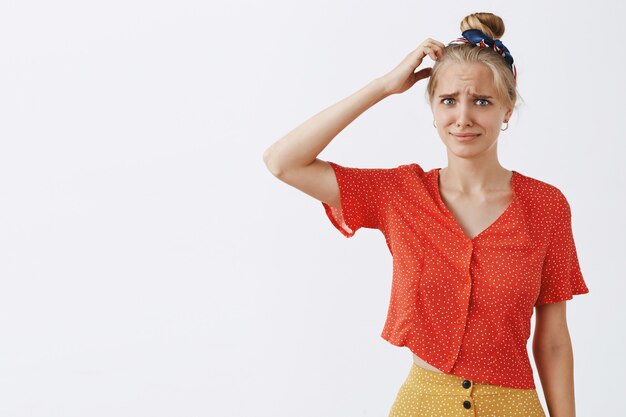 Confus et perplexe jeune fille blonde posant contre le mur blanc