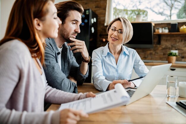 Conseiller financier souriant utilisant un ordinateur portable lors d'une réunion avec un jeune couple.