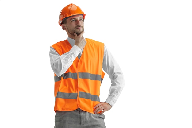 Le constructeur dans un gilet de construction et un casque orange debout sur un mur blanc. Spécialiste de la sécurité, ingénieur, industrie, architecture, gestionnaire, profession, homme d'affaires, concept d'emploi