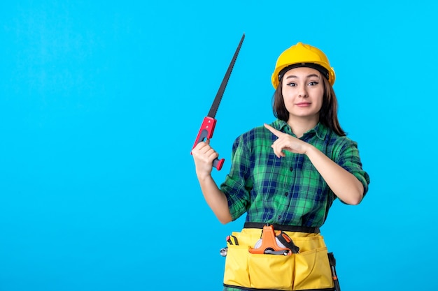 Constructeur féminin de vue de face tenant la petite scie sur le bleu