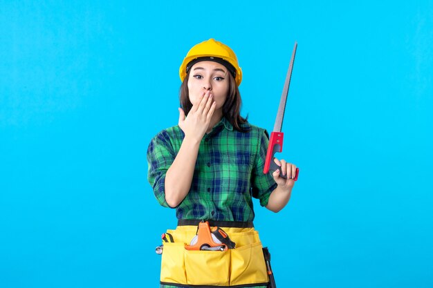 Constructeur féminin de vue de face tenant la petite scie sur le bleu