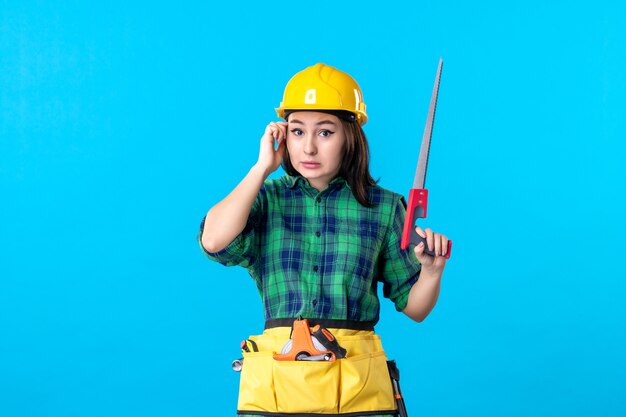 Constructeur féminin de vue de face tenant la petite scie sur le bleu