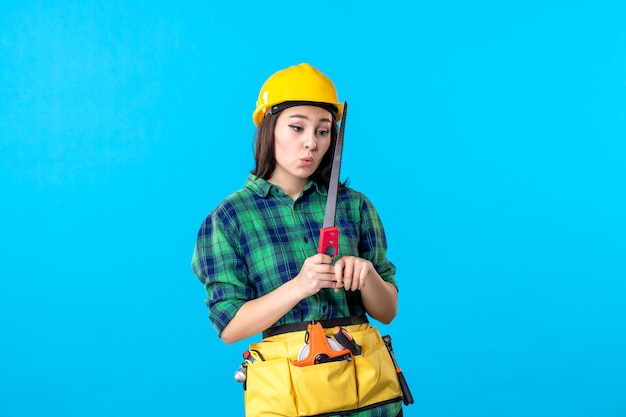Constructeur féminin de vue de face tenant la petite scie sur le bleu