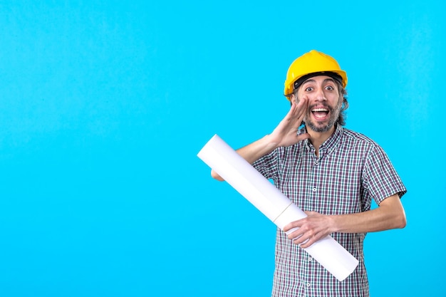 Constructeur masculin de vue de face dans le casque jaune avec le plan sur l'ingénieur de travailleur de propriété d'emploi d'architecture de bâtiment de fond bleu