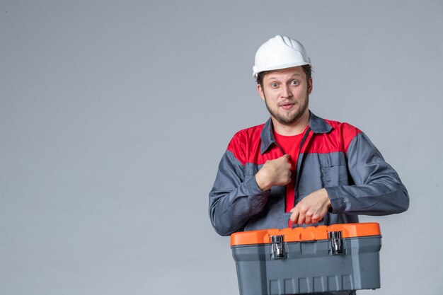 constructeur masculin vue de face en uniforme tenant une trousse à outils sur fond gris