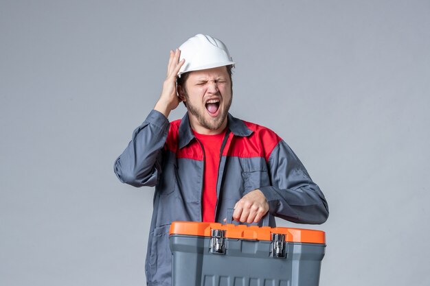 constructeur masculin vue de face en uniforme tenant une trousse à outils sur fond gris