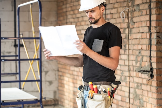 Constructeur avec des outils de construction au chantier de construction, à la recherche de plan