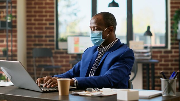 Consultant de bureau planifiant des statistiques financières sur un ordinateur portable pendant la pandémie de coronavirus. Assistant exécutif utilisant les informations du réseau sur l'application de site Web en ligne pour créer une stratégie commerciale.