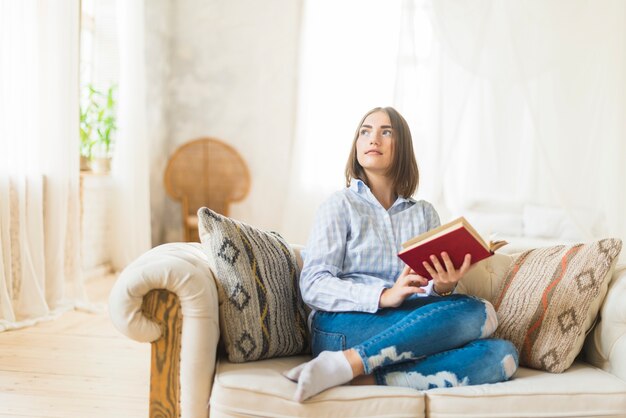 Contemplated jeune femme tenant le livre assis sur le canapé