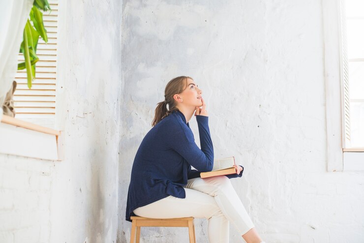 Photo gratuit contemplated jeune femme tenant le livre assis sur un tabouret