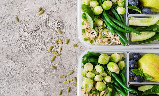 Contenants de préparation de repas verts végétaliens avec riz, haricots verts, choux de Bruxelles, concombre et fruits.