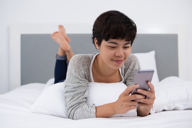 Content Asian Girl utilisant un téléphone intelligent sur le lit