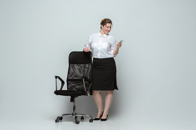 Content. Jeune femme en tenue de bureau. Personnage féminin Bodypositive, féminisme, s'aimer, concept de beauté. Femme d'affaires de grande taille sur mur gris. Patron, magnifique. Inclusion, diversité.