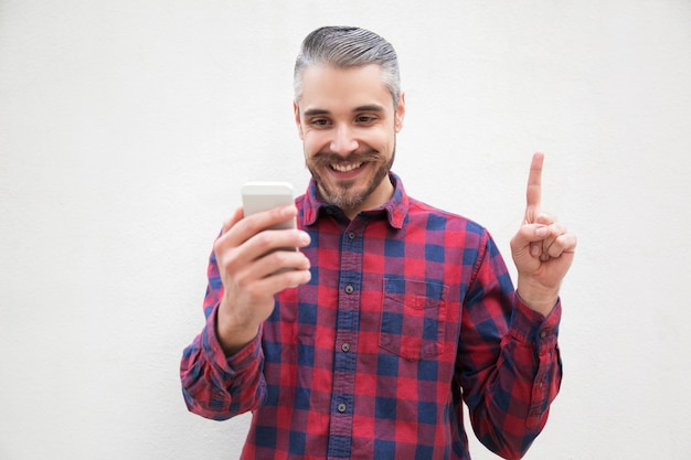 Contenu homme avec smartphone pointant vers le haut avec le doigt