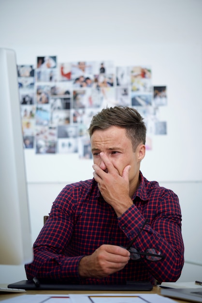 Contrarié jeune homme regardant un écran d'ordinateur, couvrant le visage avec la main et pleurant