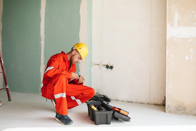 Contremaître en vêtements de travail orange et casque jaune choisissant judicieusement des outils pour le travail