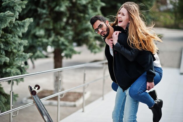 Cool couple multiracial posant avec longboard fille européenne a sauté par-dessus l'épaule homme arabe